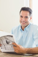 Fototapeta na wymiar Smiling casual man with newspaper in kitchen