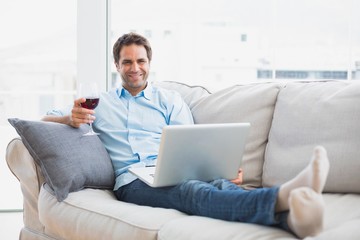 Smiling handsome man relaxing on sofa with glass of red wine