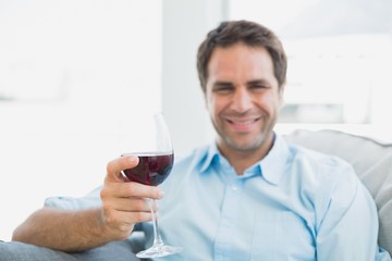 Cheerful man relaxing on sofa with glass of red wine
