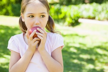 Pretty young girl eating apple in park