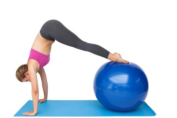 Fototapeta na wymiar Side view of a fit young woman stretching on fitness ball