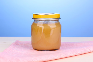 Jar of baby puree on napkin on blue background