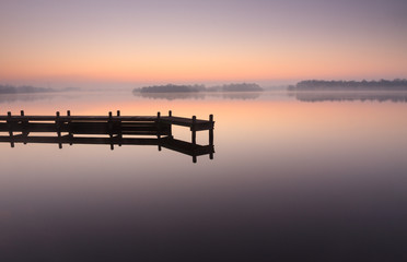 Jetty during a tranquil, foggy dawn at a lake.