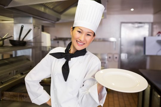 Smiling female cook holding empty plate in kitchen