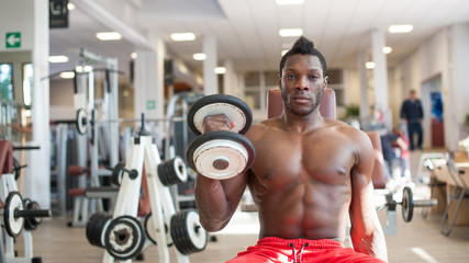 Fototapeta na wymiar Strong black man exercising with dumbbells in the gym.