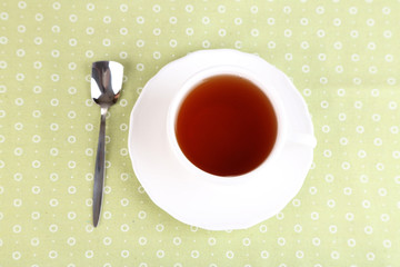 Cup with hot drink and spoon on colorful tablecloth background