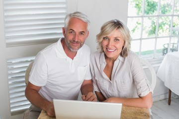 Fototapeta na wymiar Smiling mature couple using laptop at home