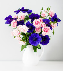 Bouquet of pink roses and blue anemones in white vase on grey ba