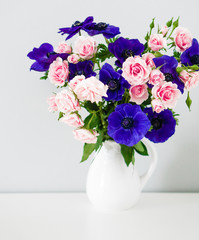Bouquet of pink roses and blue anemones in white vase on grey ba