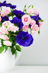 Fototapeta premium Bouquet of pink roses and blue anemones in white vase