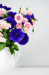 Bouquet of pink roses and blue anemones in white vase on grey ba