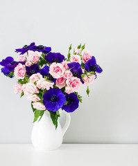 Bouquet of pink roses and blue anemones in white vase