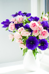 Fototapeta na wymiar Bouquet of pink roses and blue anemones in white vase near the w