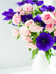 Bouquet of pink roses and blue anemones in white vase near the w