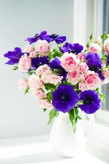 Bouquet of pink roses and blue anemones in white vase