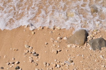 Sandy beach with pebbles and wave as background