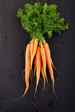 Bunch of fresh carrots with green leaves over wooden background.