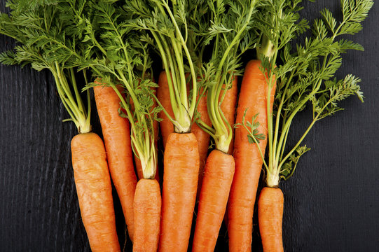 Bunch of fresh carrots with green leaves over wooden background.