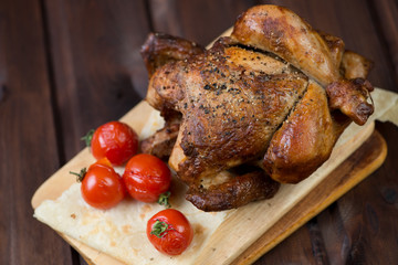 Whole baked chicken and tomatoes, wooden background, close-up