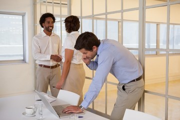 Businessman using laptop with colleagues shaking hands in