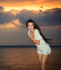 Pretty female standing near ocean in rays of sunset