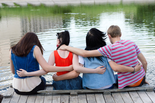 Young teenage friends sitting on bridge at river
