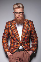 smiling fashion model with long beard leaning against gray wall