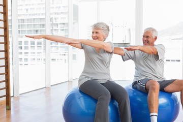 Naklejka premium Senior couple doing stretching exercises on fitness balls