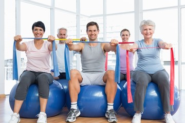 Class holding exercise belts while sitting on fitness balls