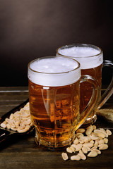 Glasses of beer with snack on table on dark background