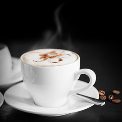 White cup of hot cappuccino on black background