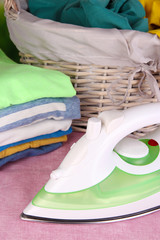 Iron and pile of colorful clothes and basket on table close up