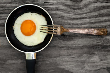 fried egg and fork on wooden background texture