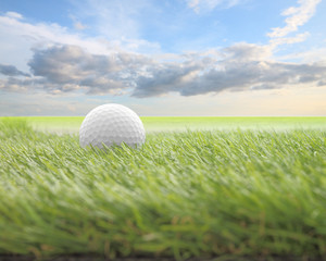 Golf ball on green front of blur cloud morning sky.