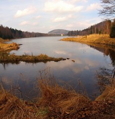 Mountain lake in forest between banks with old dry grass