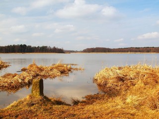 Lake between banks with old dry grass and reeds, small milestone