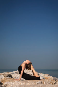 Yoga on the beach on the rocks. Rajakapotasana