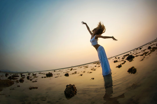 A beautiful woman is dancing on the beach at sunset