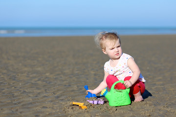 Toddler girl plays with watering can at a shore of the sea