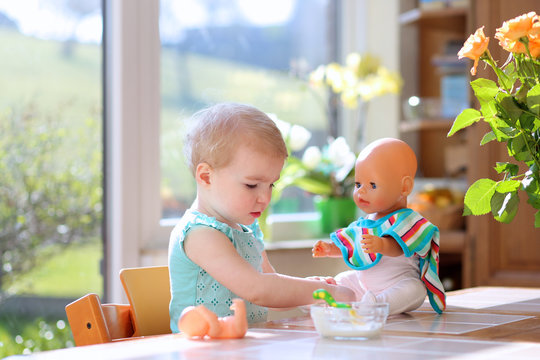  toddler girl feeding with yogurt her dolls sitting in kitchen