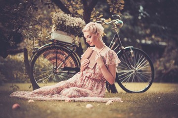 Träumende blonde Retro-Frau, die auf einer Wiese sitzt © Nejron Photo