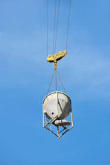 Crane lifting concrete mixer container against blue sky