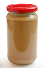 Closed glass jar of crunchy peanut butter with white background.