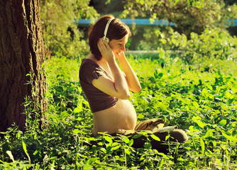 Naklejka na ściany i meble Pregnant woman listening to a music at park.
