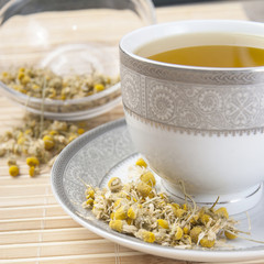 Dried camomile flowers surrounding fresh up of camomile tea