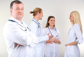 Fototapeta premium Doctor standing in front of coworkers on grey background