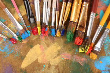 Many brushes in paints on multicolor wooden background