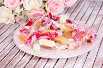 Tasty candies on plate with flowers on wooden background