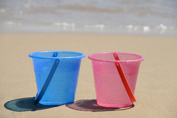 Two pink and blue buckets beach shore