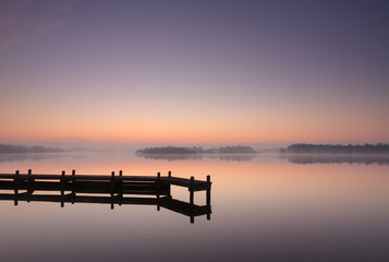 Jetty at a lake during a tranquil, foggy dawn.